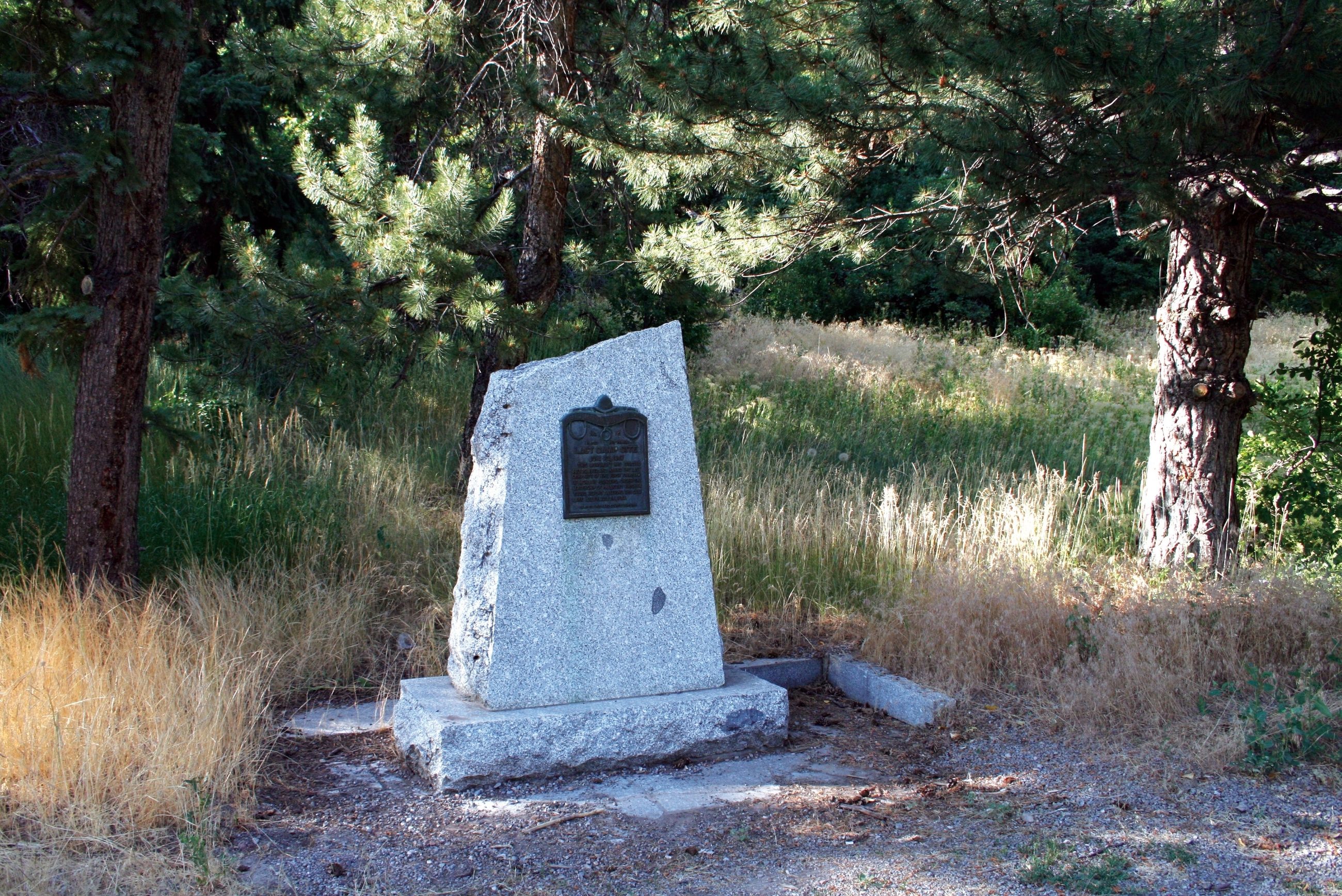 A granite trail monument with a bronze plaque marking Brigham Young's last camp on the Mormon Pioneer National Historic Trail, set among pines and golden grass
