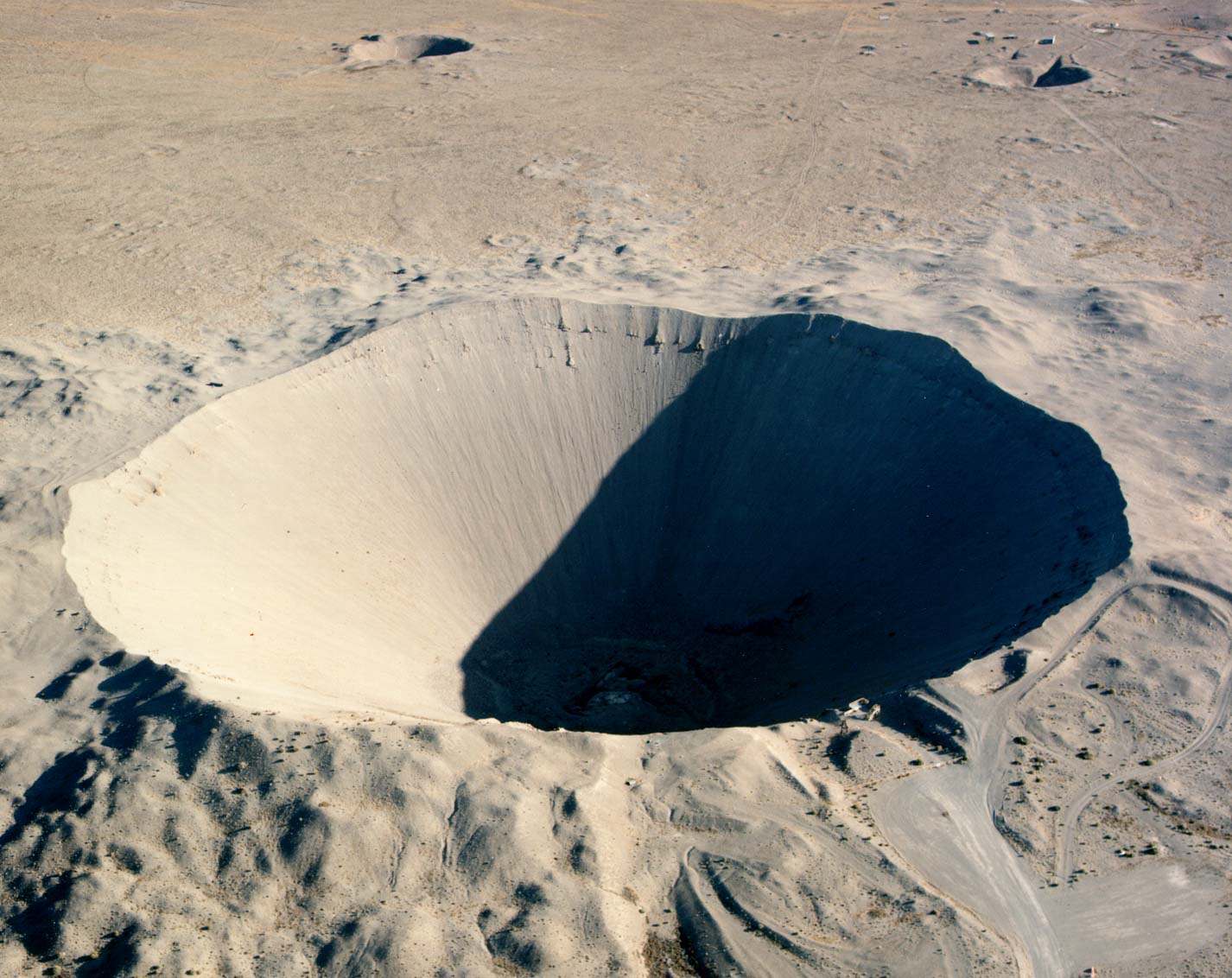 Aerial view of Sedan Crater, a vast circular blast crater in the Nevada desert left by a 1962 underground nuclear excavation test, with a viewing ramp on its rim.
