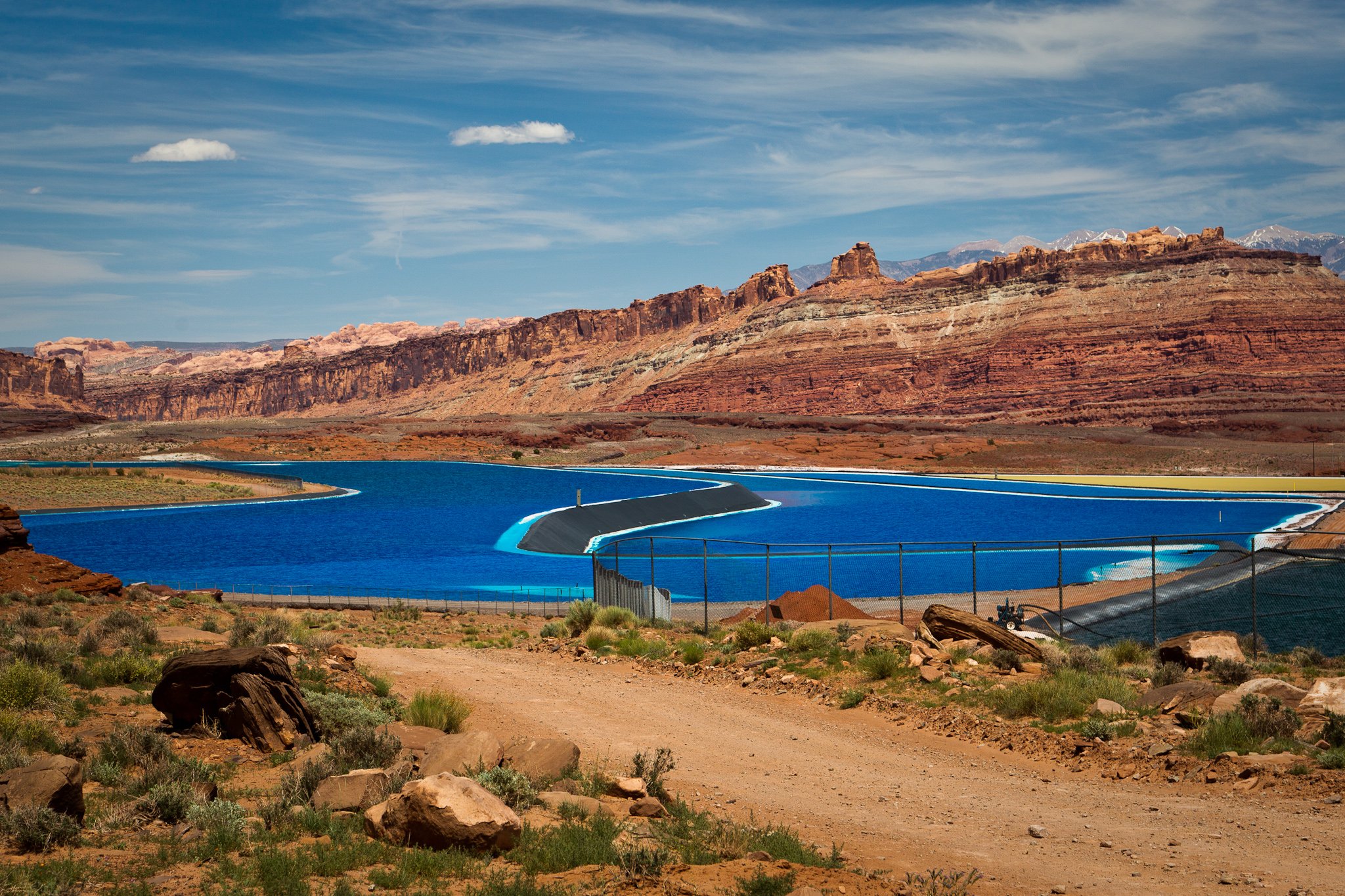 Electric-blue potash evaporation ponds set against layered red sandstone cliffs near Moab, Utah, where buried salt from an evaporated sea is pumped up and dried.