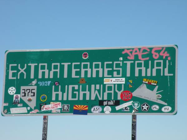 The green "Extraterrestrial Highway" sign for Nevada State Route 375, plastered with travelers' stickers and graffiti, standing against a clear desert sky.