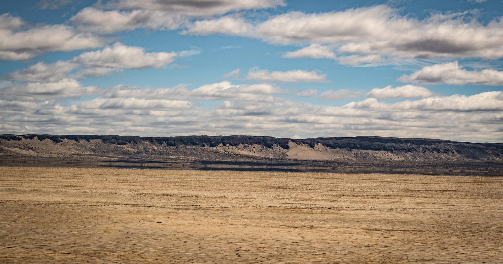 The flat, bare playa of the Alvord Desert running to a low rimrock ridge under scattered clouds