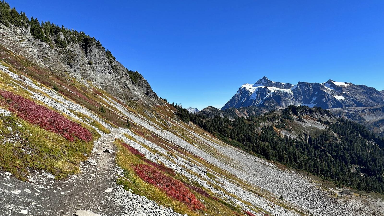 A trail across a talus slope on Ptarmigan Ridge near Artist Point, red autumn heather below and Mount Shuksan across the valley