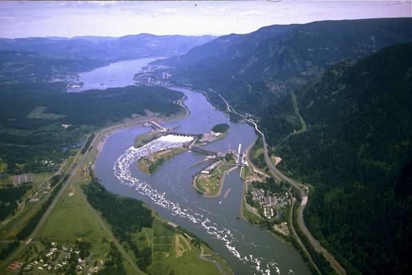 Aerial view east up the Columbia over Bonneville Lock and Dam, the spillway and powerhouses spanning the river between forested walls