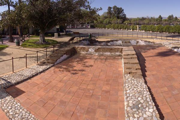 Terracotta paving and cobblestone bands at Campo de Cahuenga tracing the footprint of the original adobe, which runs on beneath Lankershim Boulevard.