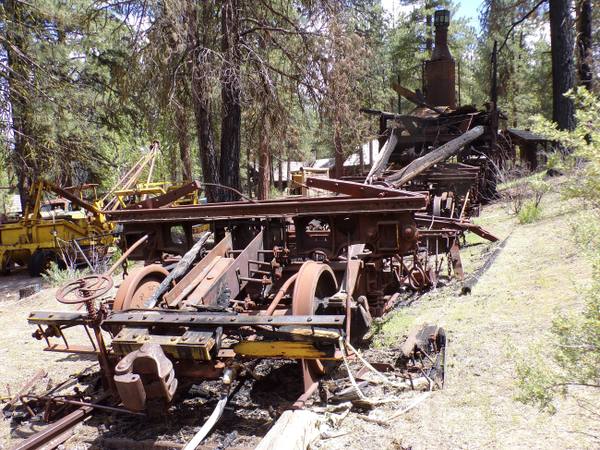 A rusted McGiffert log loader among other old logging machines under the ponderosa pines at Collier Memorial State Park