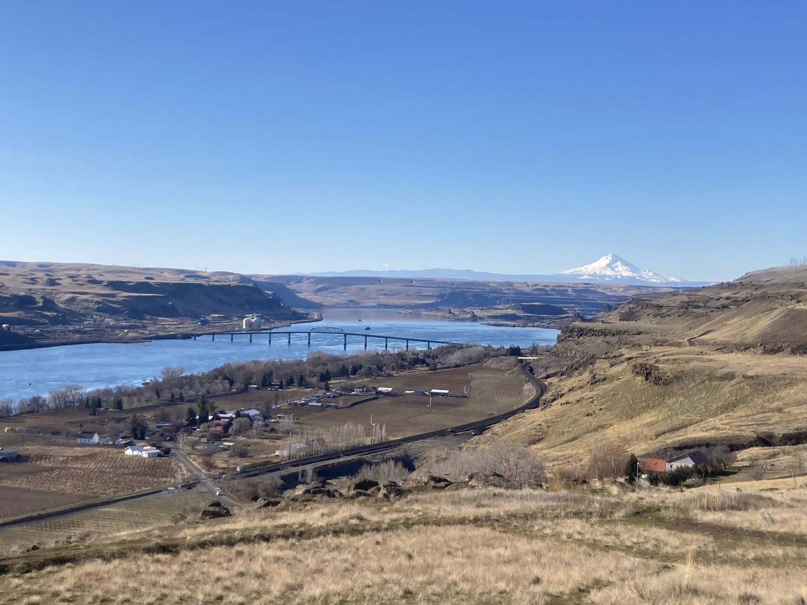 Mount Hood white on the horizon above the Columbia River east of The Dalles, dry grassland and a highway bridge in the foreground