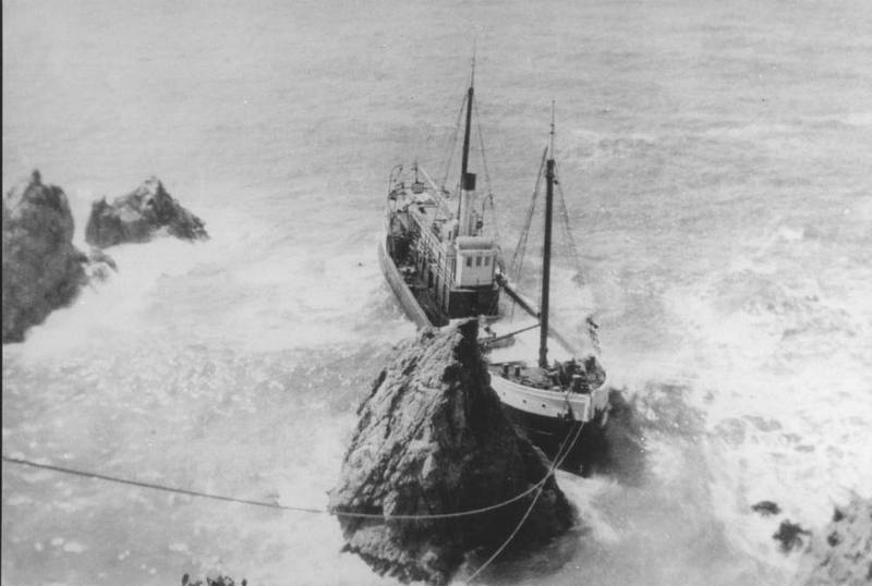 A 1909 photograph of a steam schooner hard against a sea stack in heavy surf at the Albion River on the Mendocino coast, lines running from it toward the shore, with more rocks breaking through the foam at left.