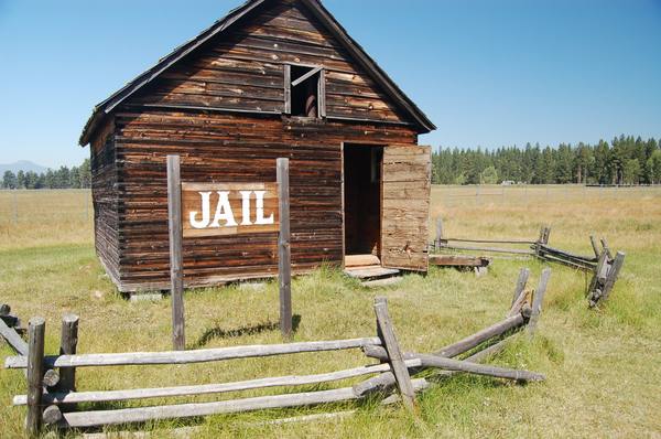 A weathered plank building signed Jail behind a split-rail fence at the Fort Klamath site in the Wood River Valley