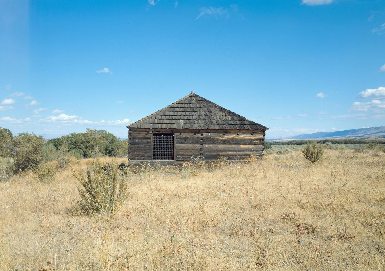 The squared-log blockhouse at Fort Simcoe in dry summer grass and sagebrush, low hills on the horizon