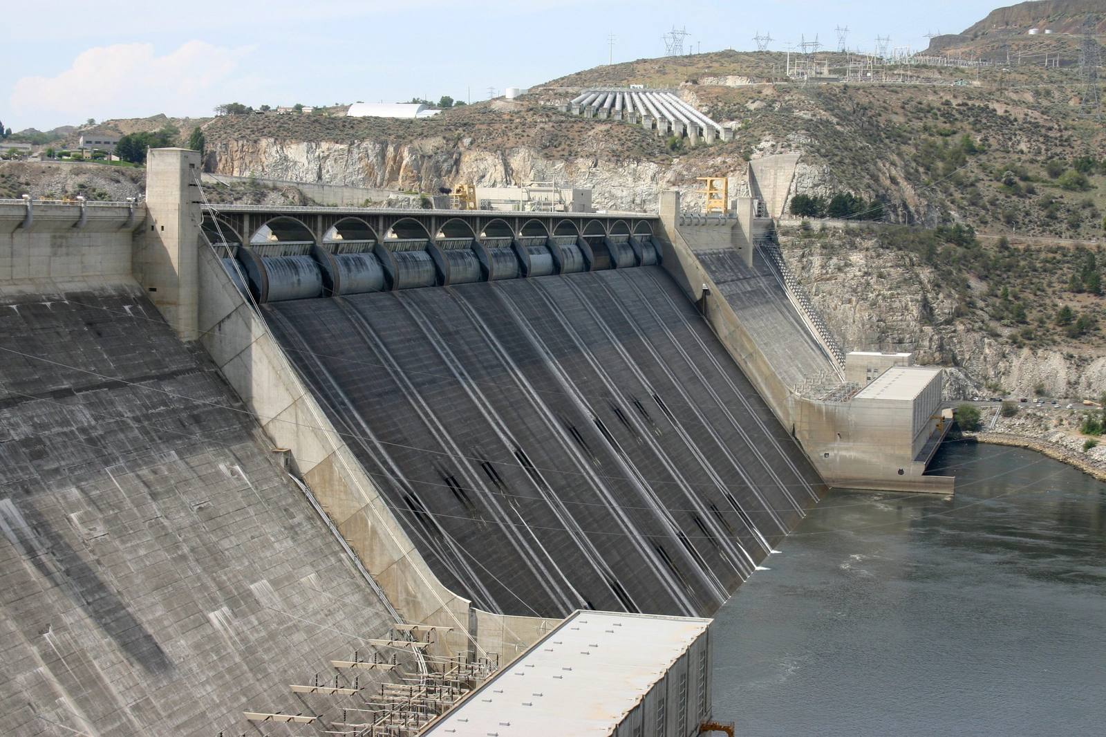 Looking down the spillway face of Grand Coulee Dam to the Columbia, the gates along its crest and the canyon wall behind