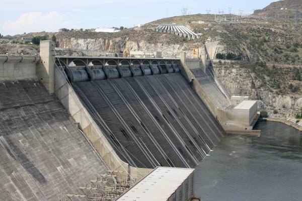 Looking down the spillway face of Grand Coulee Dam to the Columbia, the gates along its crest and the canyon wall behind