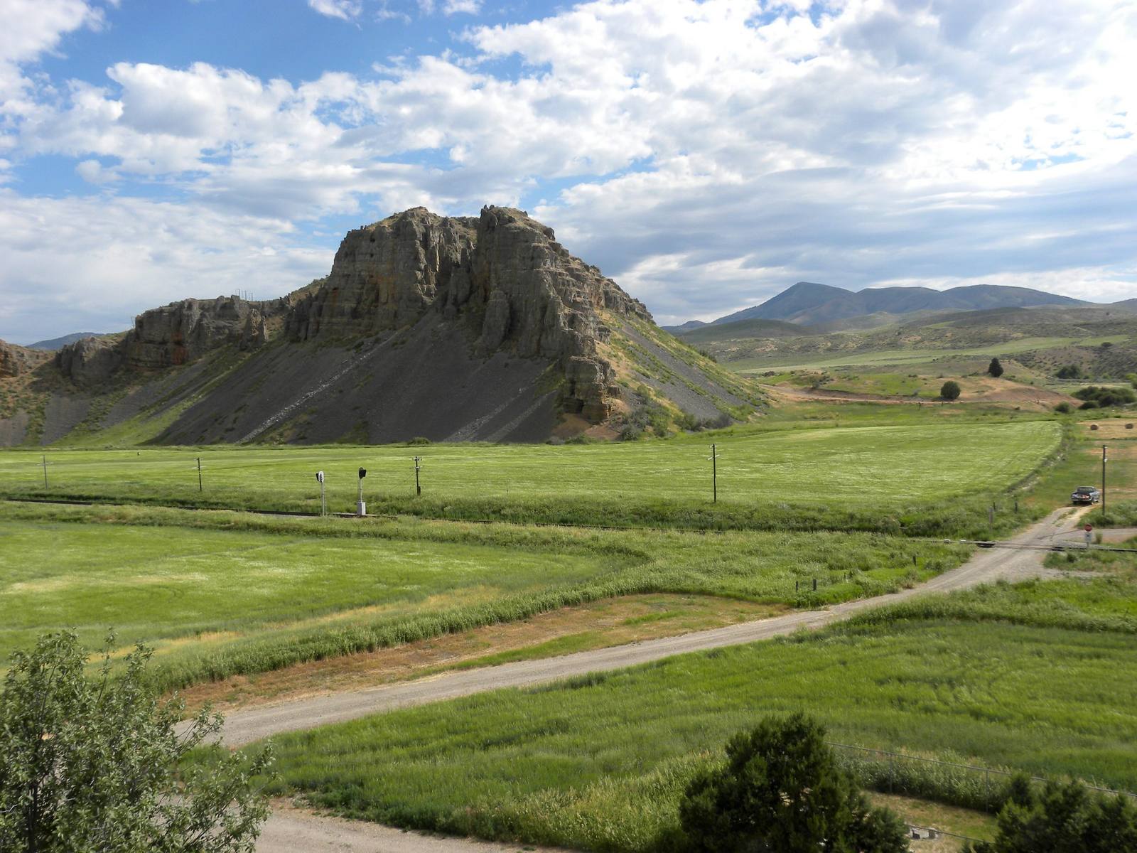 The red limestone cliff at Red Rock Pass above green fields and a gravel road