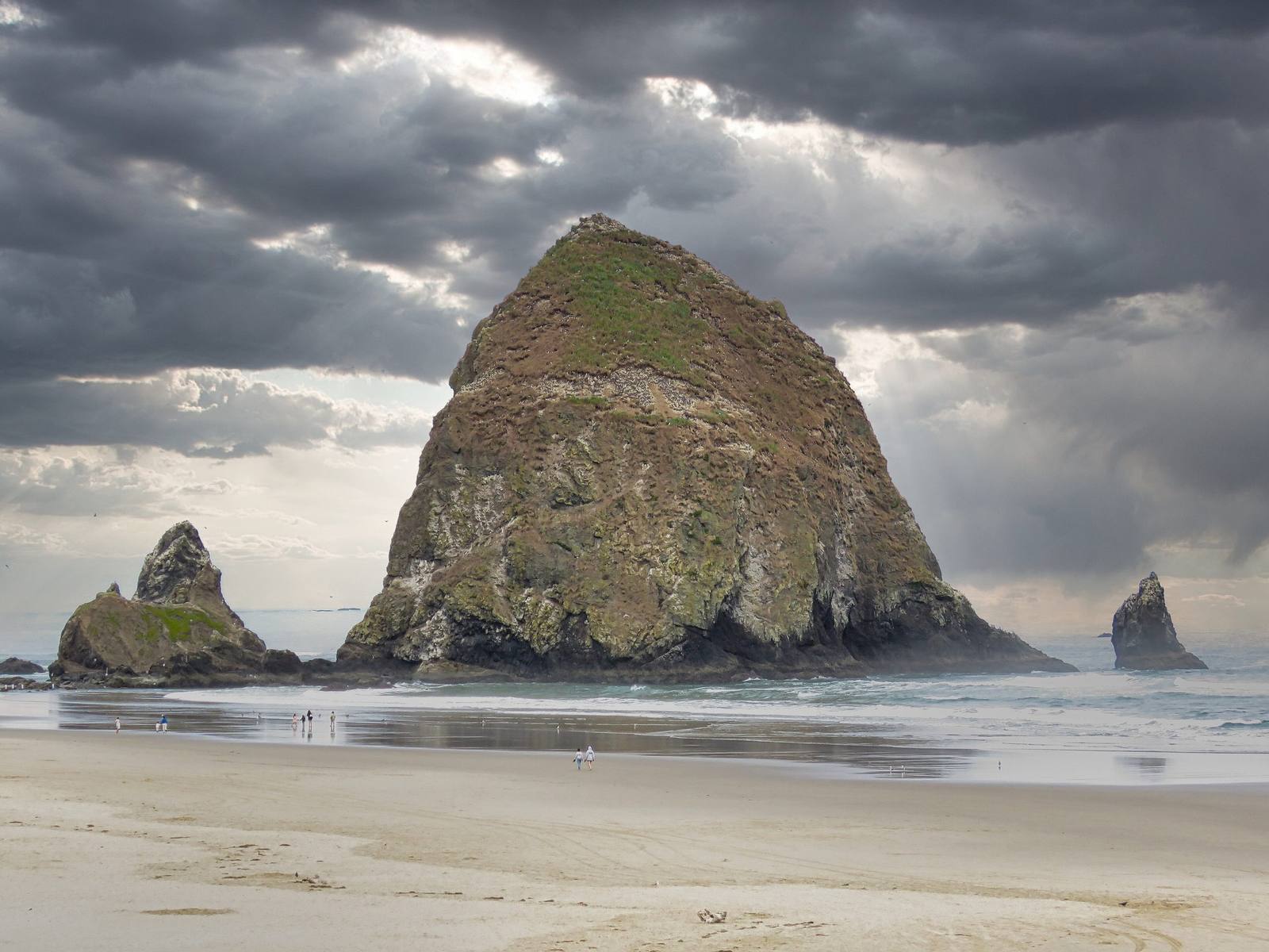 Haystack Rock and the Needles off Cannon Beach under a storm sky, the tide out across the sand