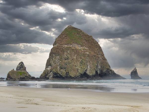 Haystack Rock and the Needles off Cannon Beach under a storm sky, the tide out across the sand