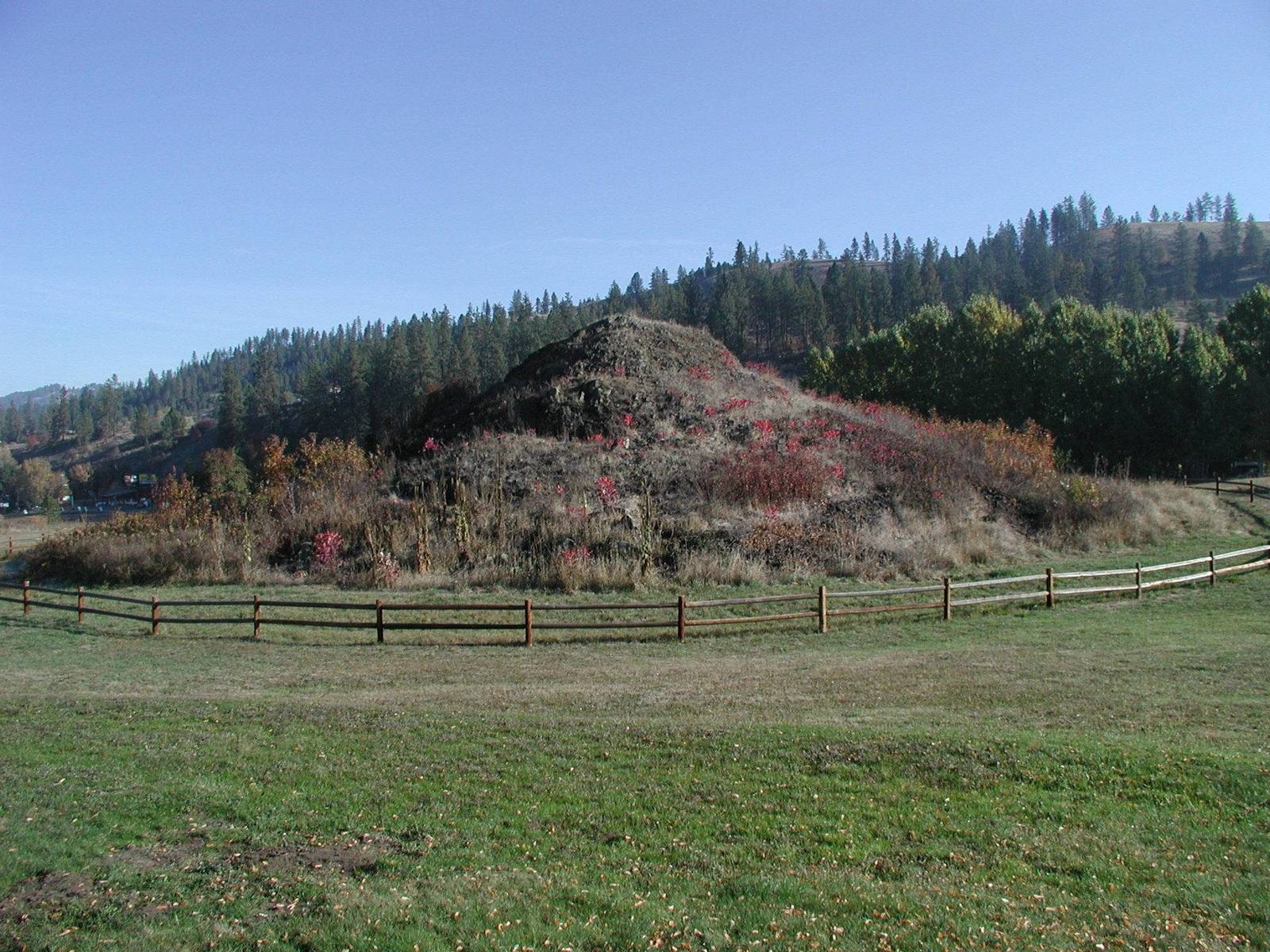 The rock mound of the Heart of the Monster behind a rail fence, with forested hills beyond