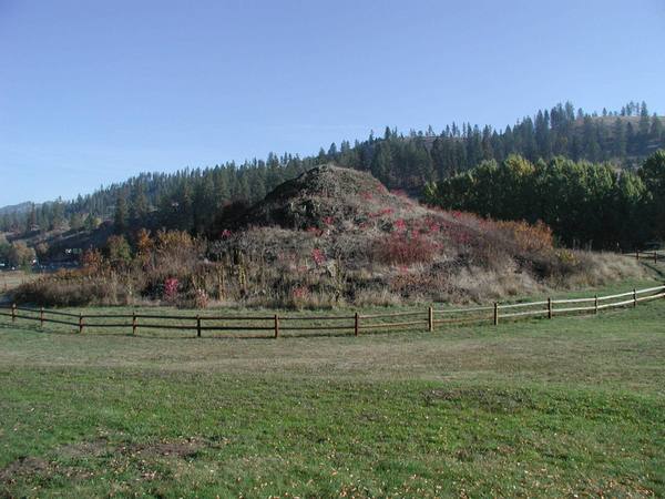 The rock mound of the Heart of the Monster behind a rail fence, with forested hills beyond