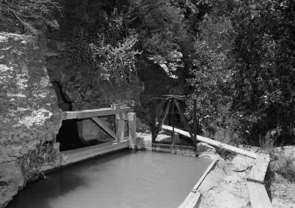 The concrete-lined Hurricane Canal running full of water into an opening cut in the cliffside in 1971, with timber control-gate frames standing over the channel