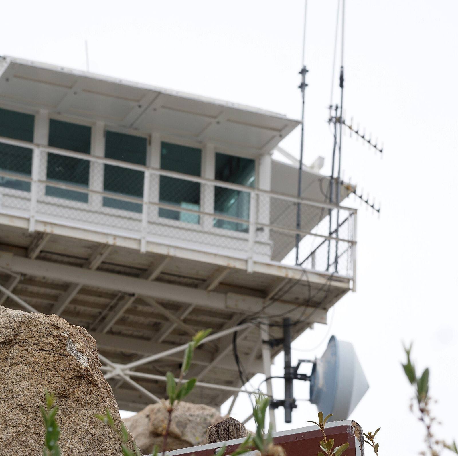 The Keller Peak fire lookout cab on its steel frame in 2018, a Forest Service sign below giving daily opening hours.