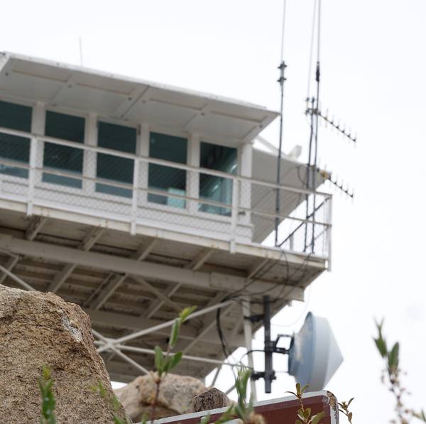 The Keller Peak fire lookout cab on its steel frame in 2018, a Forest Service sign below giving daily opening hours.