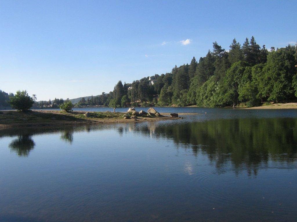 Lake Gregory at Crestline, pines and cabins along the far shore reflected in still water.