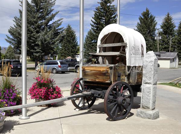 A covered wagon lettered for the National Oregon/California Trail Center beside a granite trail post in Montpelier