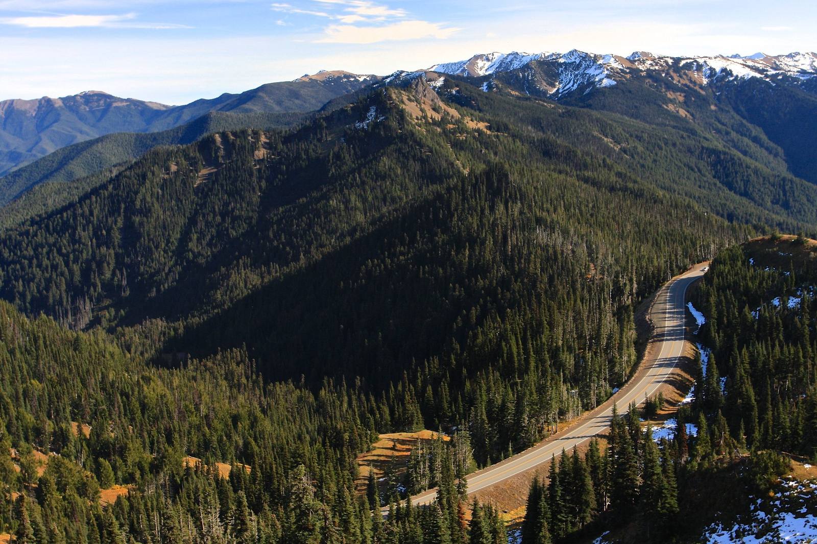 Forested ridges falling away below Hurricane Ridge toward the snow-streaked peaks of the Olympic Mountains, the Hurricane Ridge Road curving along a slope