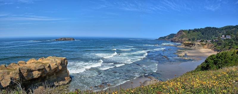Surf breaking along the central Oregon coast at Otter Rock, sandstone in the foreground and a wooded headland beyond