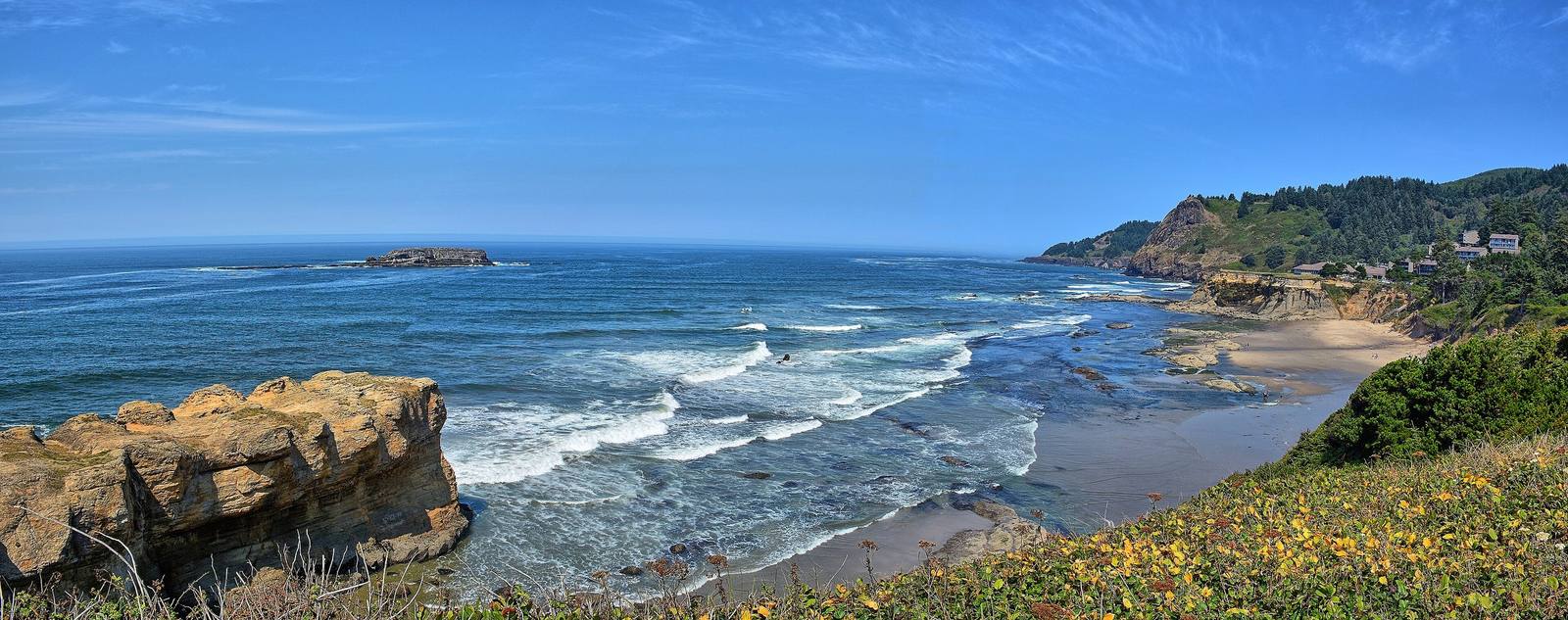 Surf breaking along the central Oregon coast at Otter Rock, sandstone in the foreground and a wooded headland beyond