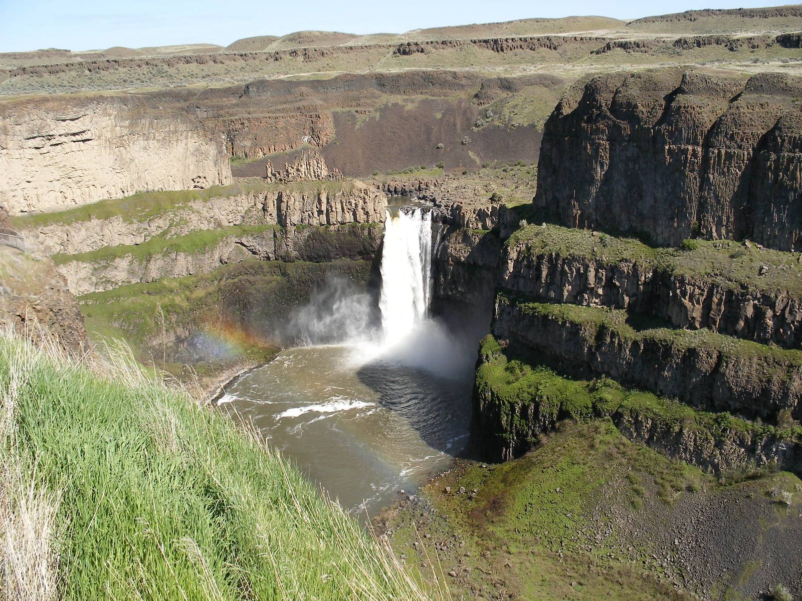 Palouse Falls dropping into its round plunge pool in a basalt canyon, a faint rainbow in the spray