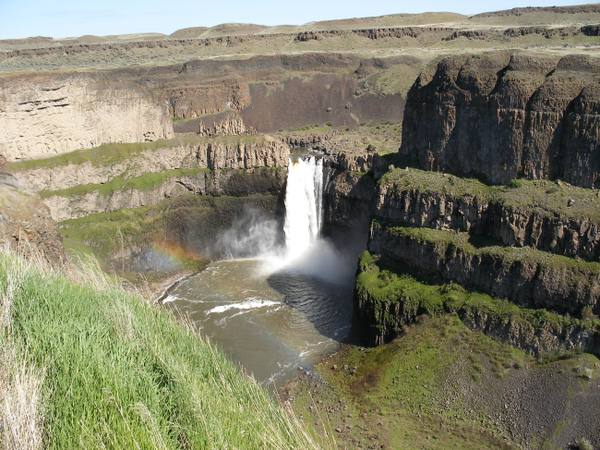 Palouse Falls dropping into its round plunge pool in a basalt canyon, a faint rainbow in the spray