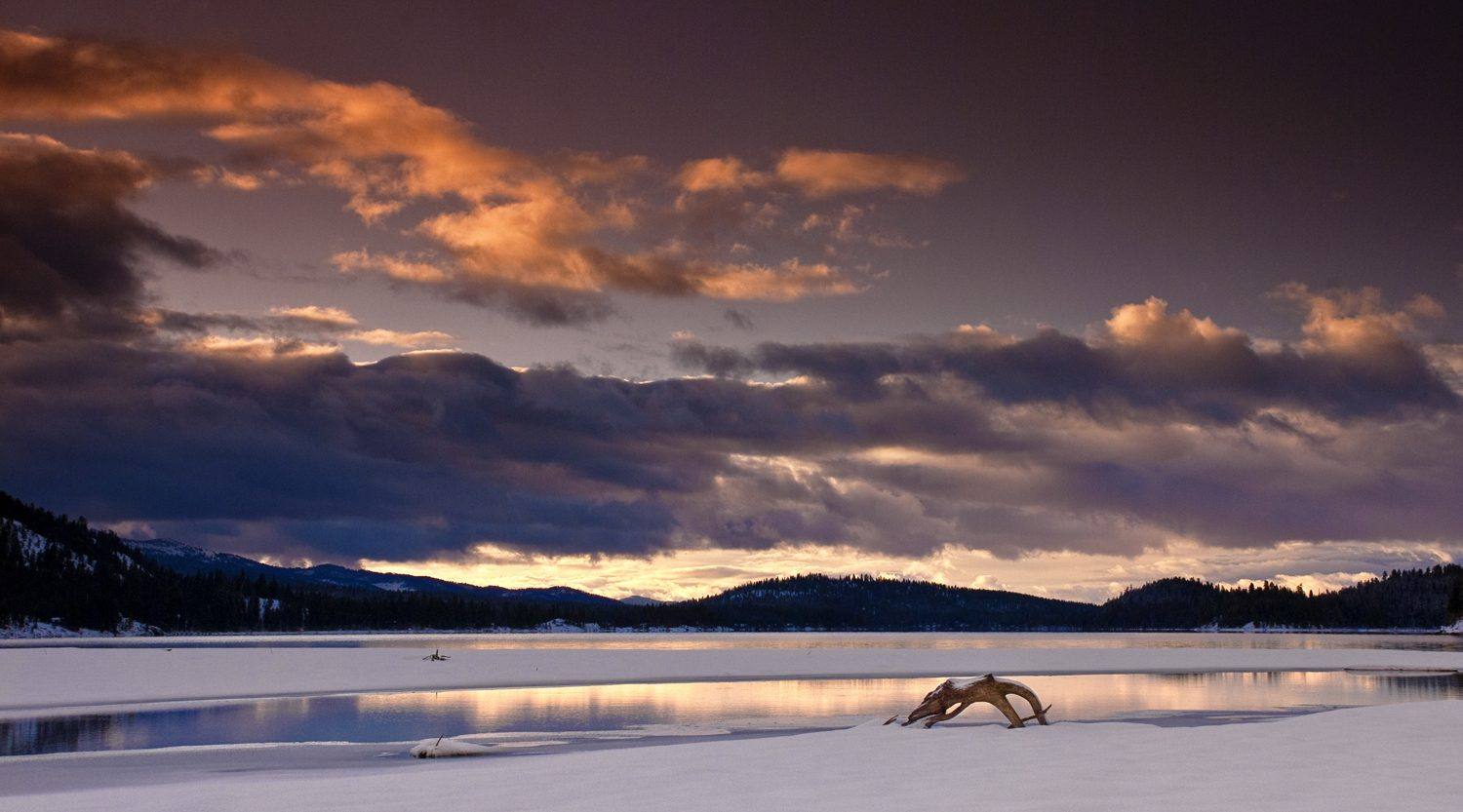 Winter sunrise over the frozen north shore of Payette Lake, forested ridges dark against the clouds