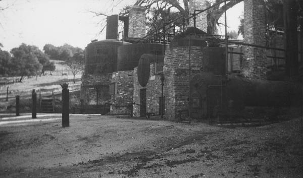 The Pioneer Oil Refinery at Newhall around 1940 — brick stills, piping and three smokestacks standing in an open field.