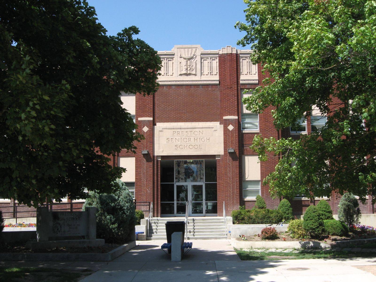The brick front of Preston Senior High School behind shade trees