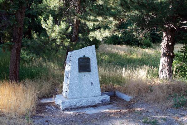 A granite trail monument with a bronze plaque marking Brigham Young's last camp on the Mormon Pioneer National Historic Trail, set among pines and golden grass