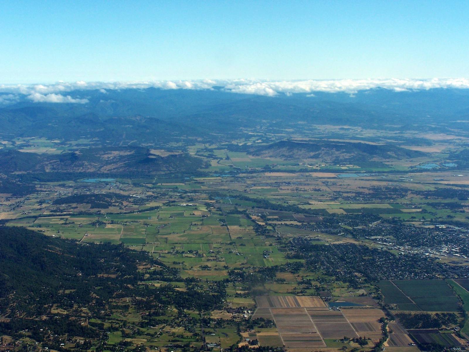 The Rogue Valley from the air, farm fields and towns spread across the valley floor below forested ridges