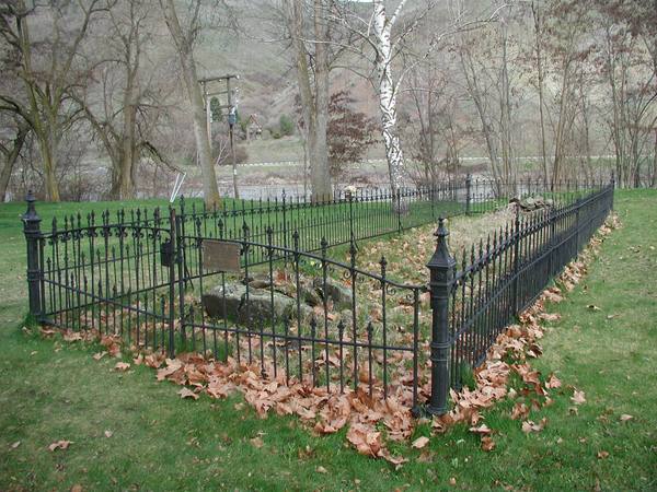 An iron fence enclosing the stone foundations of the Spalding mission house among bare cottonwoods