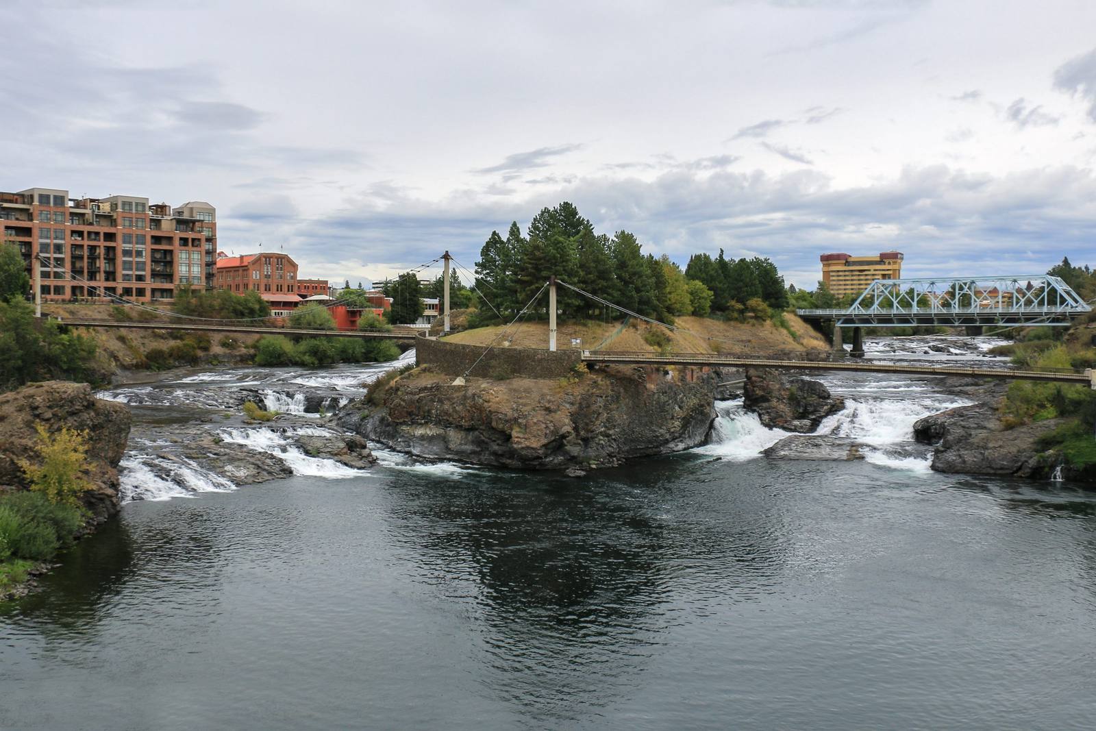 The upper falls of the Spokane River spilling over basalt ledges in Riverfront Park, footbridges and downtown buildings beyond