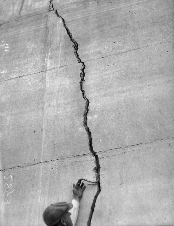A man reaching up to a crack running down a concrete face of the St. Francis Dam, photographed after the March 1928 collapse.