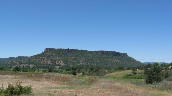 Lower Table Rock seen from the south, its flat andesite cap rimmed by cliffs above wooded slopes and dry grass