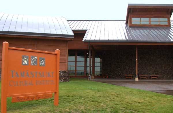 The entrance of the Tamástslikt Cultural Institute, metal roofs over timber and stone, its carved sign in the foreground