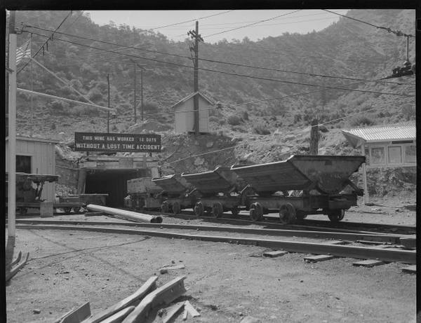 Coal cars emerging from the portal of the Castle Gate Mine in Carbon County, Utah, beneath a sign reading "this mine has worked 12 days without a lost-time accident."
