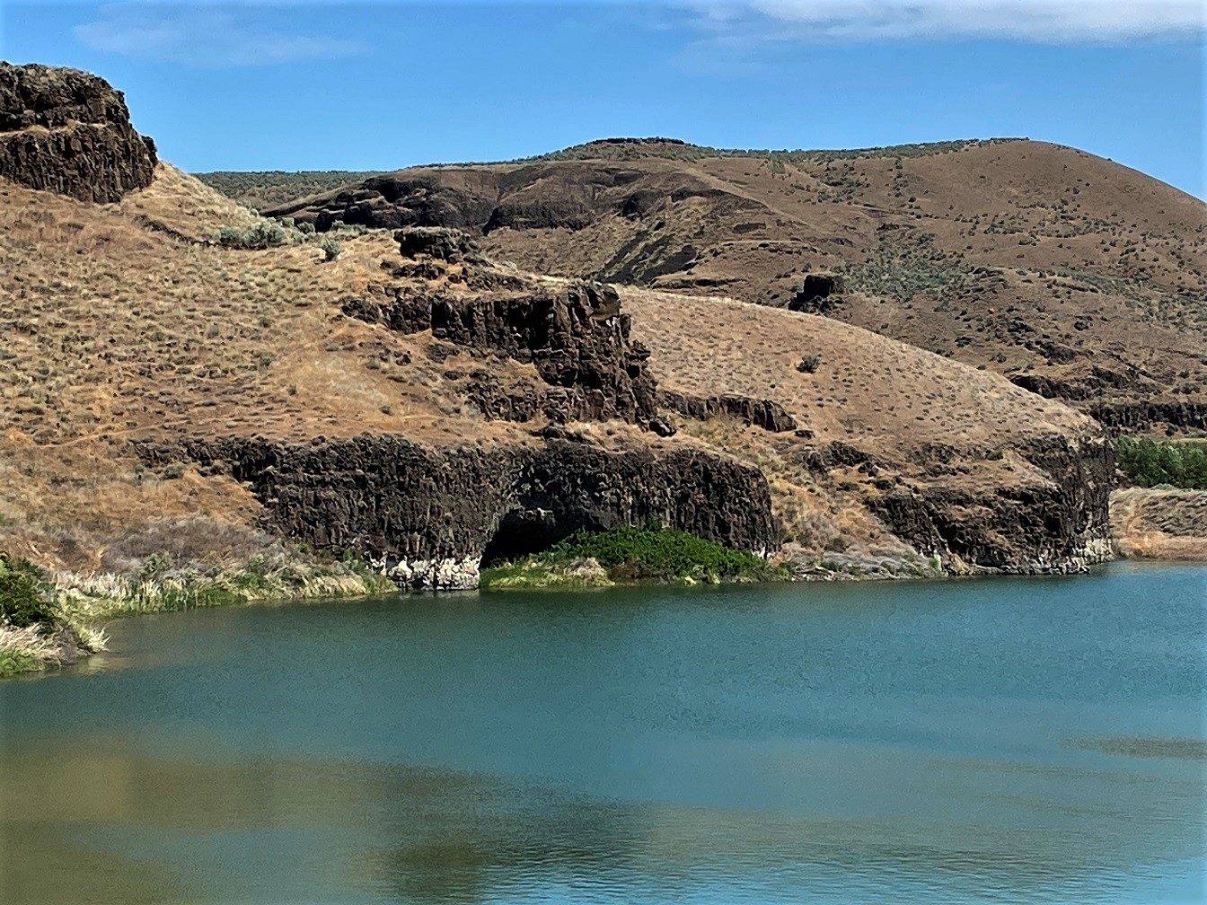 The basalt alcove of Marmes Rockshelter at the waterline of the reservoir, dry grassy canyon walls above