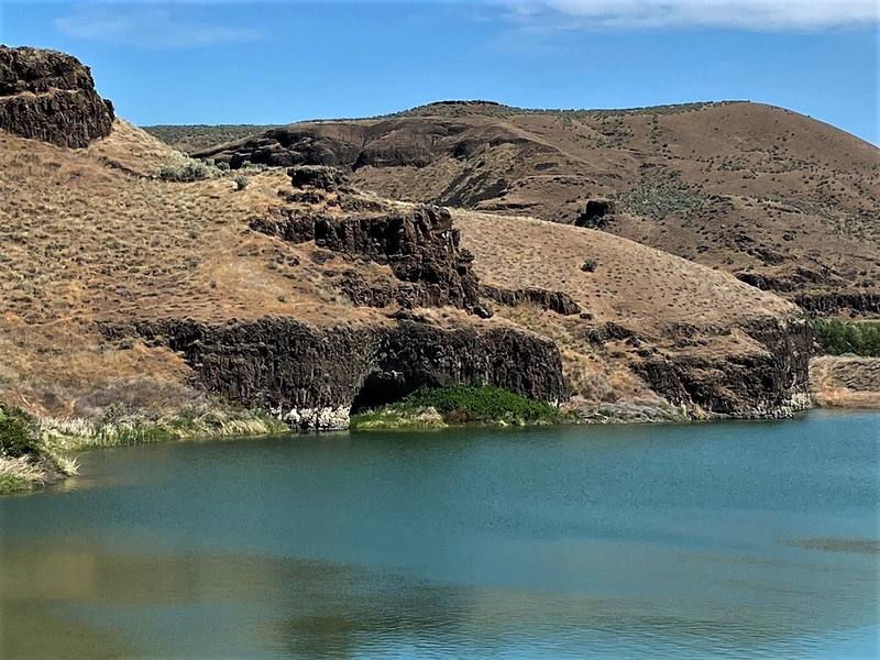 The basalt alcove of Marmes Rockshelter at the waterline of the reservoir, dry grassy canyon walls above