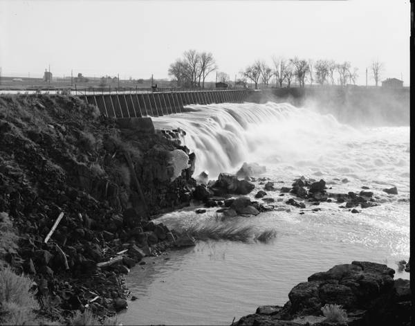 Water spilling over the gates of Milner Dam onto basalt, in a Historic American Engineering Record photograph