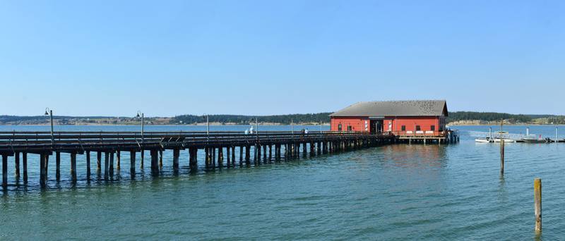 The long Coupeville wharf and its red building reaching out over the calm blue water of Penn Cove