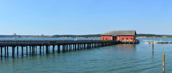 The long Coupeville wharf and its red building reaching out over the calm blue water of Penn Cove