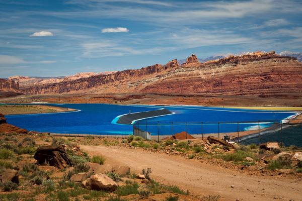 Electric-blue potash evaporation ponds set against layered red sandstone cliffs near Moab, Utah, where buried salt from an evaporated sea is pumped up and dried.
