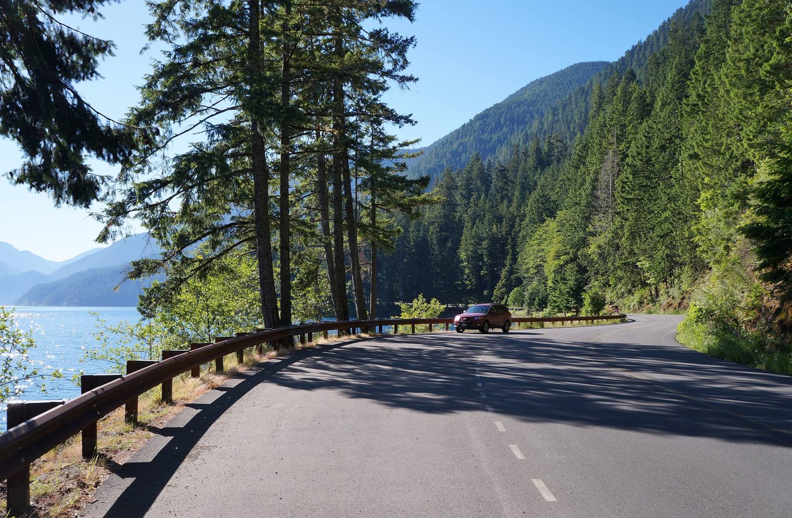 US-101 curving along the forested shore of Lake Crescent, a guardrail above the water and steep timbered slopes beyond