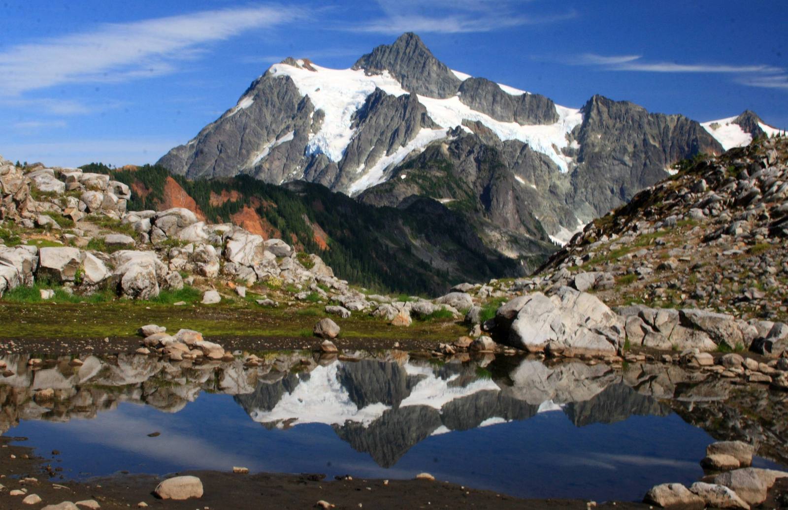 Mount Shuksan's glaciers and dark rock ridges mirrored in a still tarn among pale granite boulders near Artist Point in the North Cascades
